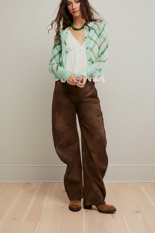 A woman wearing a mint green knit cardigan, the Free People Highland Mist Cardi, with diagonal plaid stripes in olive green and tan, styled over a white ruffled blouse and brown pants.